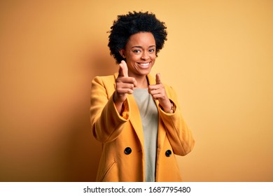 Young beautiful African American afro businesswoman with curly hair wearing yellow jacket pointing fingers to camera with happy and funny face. Good energy and vibes.