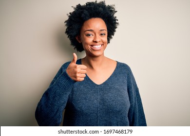 Young beautiful African American afro woman with curly hair wearing casual sweater doing happy thumbs up gesture with hand. Approving expression looking at the camera showing success.