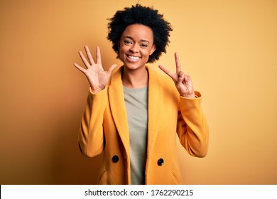 Young beautiful African American afro businesswoman with curly hair wearing yellow jacket showing and pointing up with fingers number seven while smiling confident and happy.