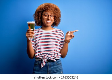 Young beautiful African American afro woman with curly hair on vacation drinking glass of beer very happy pointing with hand and finger to the side