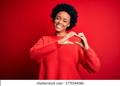 Young beautiful African American afro woman with curly hair wearing casual sweater smiling in love doing heart symbol shape with hands. Romantic concept.