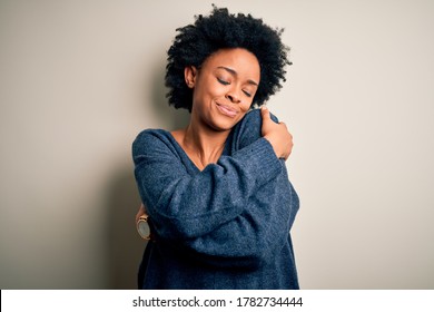 Young beautiful African American afro woman with curly hair wearing casual sweater Hugging oneself happy and positive, smiling confident. Self love and self care