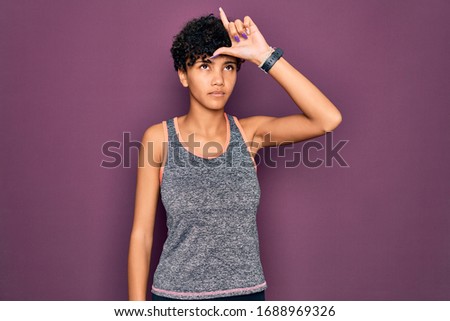 Young beautiful african american afro sportswoman doing exercise wearing sportswear making fun of people with fingers on forehead doing loser gesture mocking and insulting.