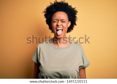 Young beautiful African American afro woman with curly hair wearing casual t-shirt sticking tongue out happy with funny expression. Emotion concept.