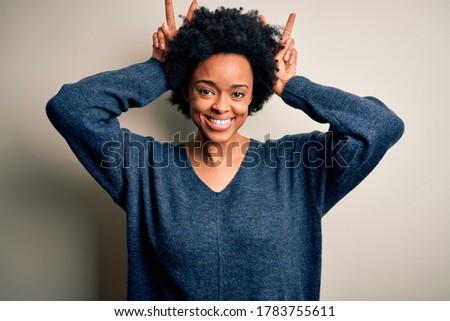 Young beautiful African American afro woman with curly hair wearing casual sweater Posing funny and crazy with fingers on head as bunny ears, smiling cheerful