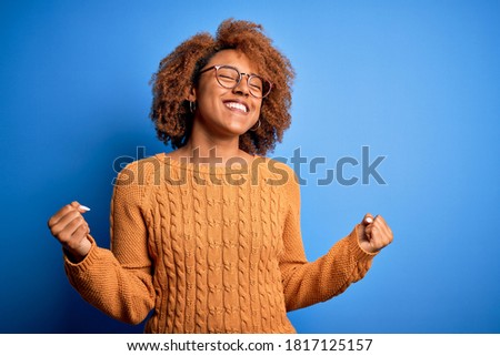 Young beautiful African American afro woman with curly hair wearing casual sweater very happy and excited doing winner gesture with arms raised, smiling and screaming for success. Celebration concept. Foto d'archivio © 