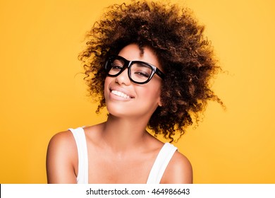 Young beautiful african american girl with an afro hairstyle. Laughing girl wearing eyeglasses. Portrait. Yellow background. Girl looking at camera.