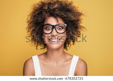 Young beautiful african american girl with an afro hairstyle. Attractive girl wearing eyeglasses. Portrait. Cute toothy smile.Yellow background.