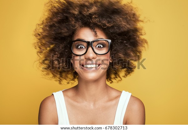アフロの髪型をした若い美しいアフリカ系アメリカ人の女の子 眼鏡をかけた魅力的な女の子 ポートレート 黄色い背景にかわいい歯の笑み の写真素材 今すぐ編集