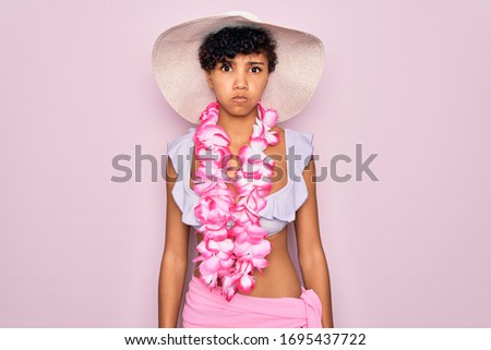 Young beautiful african american tourist woman wearing bikini and hawaiian lei flowers puffing cheeks with funny face. Mouth inflated with air, crazy expression.