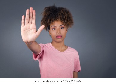 Young beautiful African American woman doing stop gesture with palm of the hand. Warning expression with negative and serious gesture on the face isolated over gray background.