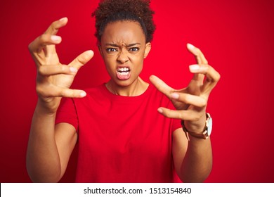 Young Beautiful African American Woman With Afro Hair Over Isolated Red Background Shouting Frustrated With Rage, Hands Trying To Strangle, Yelling Mad