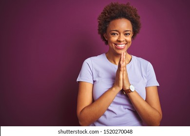 Young Beautiful African American Woman With Afro Hair Over Isolated Purple Background Praying With Hands Together Asking For Forgiveness Smiling Confident.