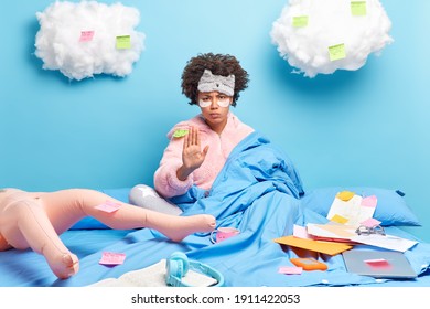 Young Beautiful African American Woman In Cozy Sweater And Sleepmask Makes Refusal Gesture Does Paperwork At Home Poses On Comfortable Bed Inflated Doll As Imaginary Friend Says No Stop There