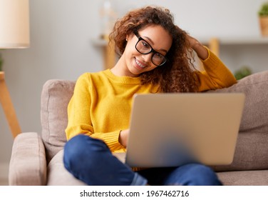 Young beautiful african american woman wearing eyeglasses working remotely on laptop while sitting on sofa at home, cheerful female student studying online. Distance education and freelance concept - Powered by Shutterstock