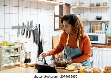 Young Beautiful African American Woman In Kitchen Learning Online Virtual Cooking Class From Tablet Computer At Home