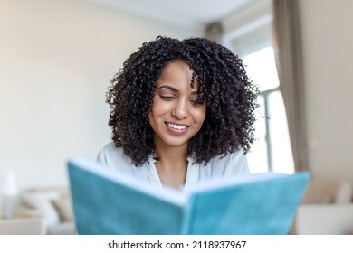 Young Beautiful African American Woman Holding Book, University Student Studying, Learning Language. Leisure, Literature And People Concept - Smiling African American Woman Reading Book At Home