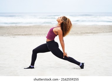 Young Beautiful African American Woman In Workout Clothing Exercises At The Beach Doing Yoga In The Crescent Moon Pose                               