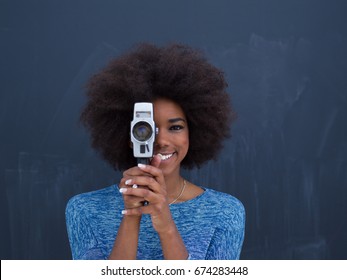 A Young Beautiful African American Woman Using A Retro Video Camera Isolated On A Gray Background