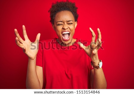 Young beautiful african american woman with afro hair over isolated red background celebrating mad and crazy for success with arms raised and closed eyes screaming excited. Winner concept