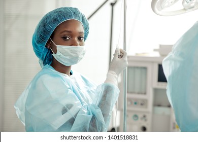 Young Beautiful African Nurse Setting The Partient's Dropper. Close Up Photo.