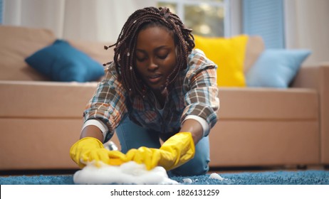 Young Beautiful African Woman Cleaning Carpet with Foam and Brush. Closeup of afro-american housewife wearing protective gloves washing carpet with detergent and brush in living room - Powered by Shutterstock