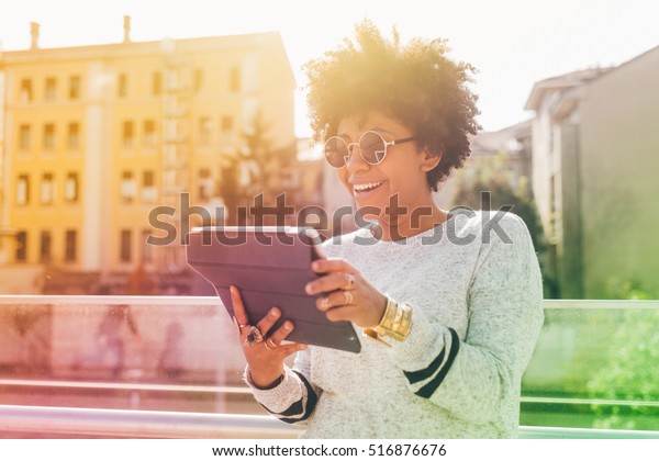 Young beautiful afro woman outdoor in city back\
light using tablet - technology, social network, communication\
concept. Colorful\
filtered.