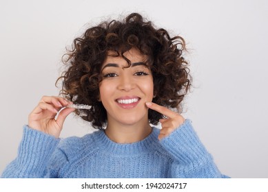 Young beautiful Arab woman holding an invisible aligner braces against white studio background and pointing to her perfect white teeth. Dental healthcare and beauty concept. - Shutterstock ID 1942024717