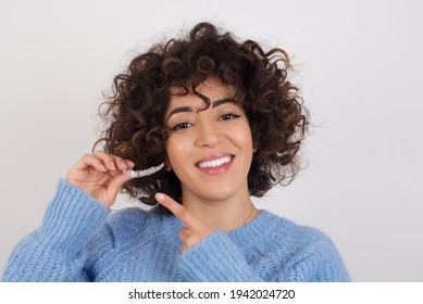 Young beautiful Arab woman holding an invisible aligner braces against white studio background and pointing at it. Dental healthcare concept. - Shutterstock ID 1942024720