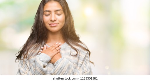Young beautiful arab woman wearing winter sweater over isolated background smiling with hands on chest with closed eyes and grateful gesture on face. Health concept. - Shutterstock ID 1183301581