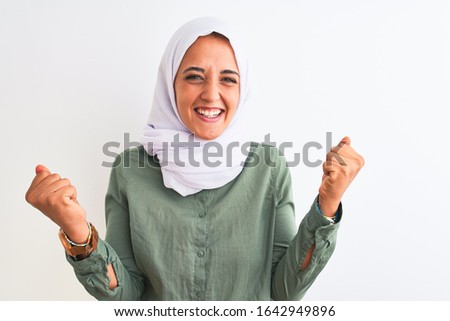 Young beautiful Arab woman wearing traditional Muslim hijab over isolated background celebrating surprised and amazed for success with arms raised and open eyes. Winner concept.