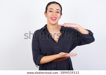 young beautiful Arab woman wearing gray dress against white studio background gesturing with hands showing big and large size sign, measure symbol.