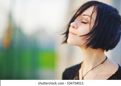 Young beautiful asian brunette woman, eyes closed, enjoying the bright warm day on blurred background close up. Air deep breath, yoga mind zen relax, calm peace pray hope concept. Light skin lady spa.