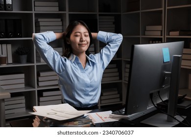 Young beautiful Asian business woman relaxing after working at her desk, working overtime at night.
