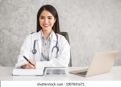 Young Beautiful Asian Doctor Woman Working Happy And Smile In Hospital, Sitting On Table, Asian Medical Concept