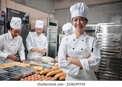 Young beautiful Asian female chef in white cooking uniform looks at camera, arms crossed and cheerful smile with food professional occupation, commercial pastry culinary jobs in a restaurant kitchen. - Powered by Shutterstock