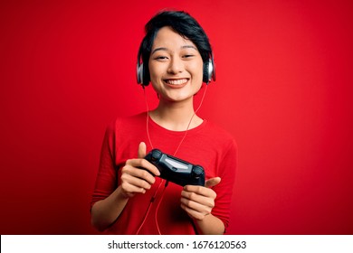 Young Beautiful Asian Gamer Girl Playing Video Game Using Joystick And Headphones With A Happy Face Standing And Smiling With A Confident Smile Showing Teeth