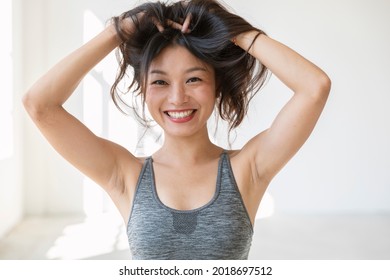 Junge schöne asiatische Mädchen lächelt und spielt mit ihrem Haar. Sie trägt einen sportlichen Oberteil und einen roten Lippenstift. isoliert