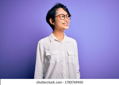 Young Beautiful Asian Girl Wearing Casual Shirt And Glasses Standing Over Purple Background Looking Away To Side With Smile On Face, Natural Expression. Laughing Confident.