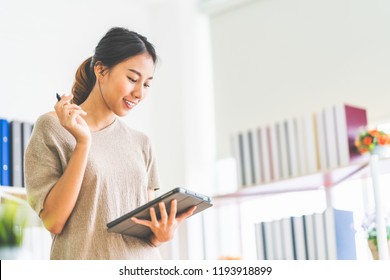 Young Beautiful Asian Girl Working At Home Office Using Digital Tablet, With Copy Space. Business Owner Entrepreneur, Small Business Startup Company, Or Casual Freelance Job Lifestyle Concept.