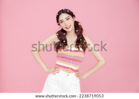 Young beautiful Asian happy cute slim woman with pigtails and perfect skin having fun and posing on pink isolated background. Stylish female model hands on waist in studio.