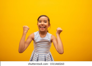 Young Beautiful Asian Little Girl Happily Rejoicing Saying Yes. Success And Achievement Concept. Cheerful Pretty Japanese Kid On Yellow Background.