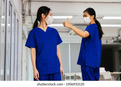 Young Beautiful Asian Medical Nurse In Scrub Uniform Wears Face Mask Admire And Give Thumbs Up To Coworker At Hospital During Covid19 Pandemic. Trust And Good Cooperation In Corporate Culture Concept