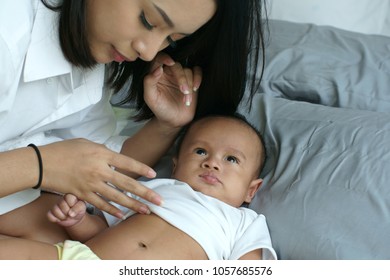 Young beautiful Asian mother caring and playing with her baby in the bedroom on a bright morning sunshine