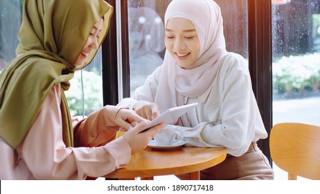 Young Beautiful Asian Muslim Women Enjoying A Relaxing Moment Working And Playing With Mobile Phone In The Coffee Shop On A Bright Sunny Day