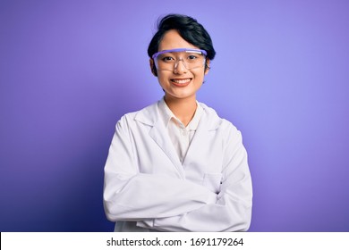 Young beautiful asian scientist girl wearing coat and glasses over purple background happy face smiling with crossed arms looking at the camera. Positive person. - Shutterstock ID 1691179264