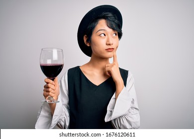 Young Beautiful Asian Sommelier Girl Drinking Glass Of Red Wine Over Isolated White Background Serious Face Thinking About Question, Very Confused Idea