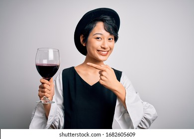 Young Beautiful Asian Sommelier Girl Drinking Glass Of Red Wine Over Isolated White Background Very Happy Pointing With Hand And Finger