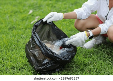 Young beautiful asian volunteer woman hands holding garbage bag and picking up litter while cleaning plastic bottle from lawn during a volunteering environmental cleanup area park event outdoors - Powered by Shutterstock