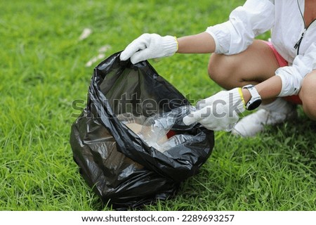 Young beautiful asian volunteer woman hands holding garbage bag and picking up litter while cleaning plastic bottle from lawn during a volunteering environmental cleanup area park event outdoors